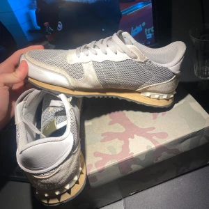 Valentino Garavani sneakers - Snygga Valentino rockrunners i beige och grått med vita detaljer. Skorna har en stilren design med snörning och en bekväm sula. Perfekta för en trendig look. Skorna är i nytt skick och letar efter en ny ägare!