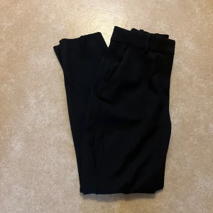 Svarta kostymbyxor från H&M - Snygga svarta kostymbyxor från H&M i storlek 34. De är aldrig använda. De har en ficka på varje sida och bak på ser det ut som fickor men det är inte det(se bilden) de är inte högmidjade men inte för lågmidjade 