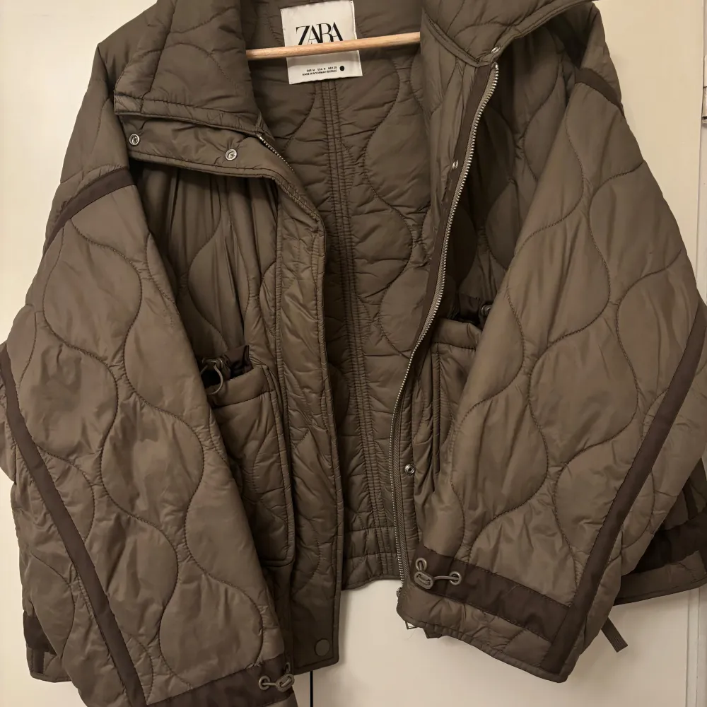 Säljer en grön quiltad jacka från Zara med dragkedja och knappar. Jackan har en oversized passform och långa ärmar. Perfekt för höst och vår med sin stilrena design och bekväma material.. Takit.