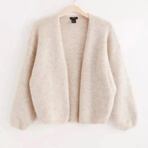 Beige kofta från Lindex  - Mysig beige kofta från Lindex  i en mjuk och fluffig kvalitet. Koftan har en öppen design utan knappar och långa ärmar, perfekt för lager-på-lager under kyliga dagar. Helt oanvänd men saknar prislapp 