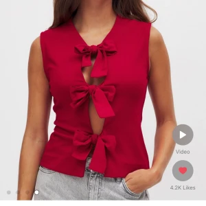 Röd ärmlös topp med rosetter - Snygg röd ärmlös topp med tre stora rosetter framtill. Perfekt för en trendig look. Passar bra till jeans eller kjol. Helt ny med prislapp!!