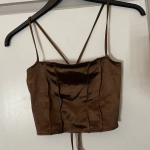 Brun korsettopp från H&M Divided - Snygg brun korsettopp från H&M Divided med smala axelband och snörning i ryggen. Perfekt för en trendig look.