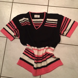 Randig stickad tröja med v-ringning - Säljer en snygg stickad tröja med v-ringning i svart, rosa och vit. Tröjan har korta ärmar och ett randigt mönster som ger en cool look. Perfekt för en avslappnad stil.