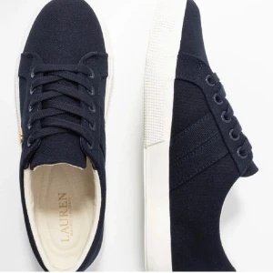 Svarta sneakers från Ralph Lauren - Snygga marin blåa sneakers från Lauren Ralph Lauren med vit sula och diskret guldfärgad logga på sidan. Skorna har snörning och är tillverkade i textilmaterial, vilket ger en stilren och modern look. Priset kan diskuteras!! Skriv för egna bilder på skorna💓