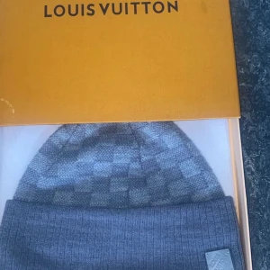  Louis Vuitton Mössa - Snygg grå mössa från Louis Vuitton med ett diskret rutigt mönster. Mössan är stilren och passar perfekt för kyligare dagar. Den kommer i en elegant förpackning.
