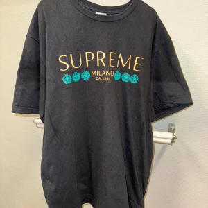 Svart t-shirt från Supreme | Large - Snygg svart t-shirt från Supreme med tryck i gult och turkost. Texten 'SUPREME MILANO DAL 1994' pryder framsidan. Tillverkad i 100% bomull för en skön känsla. Från SS21