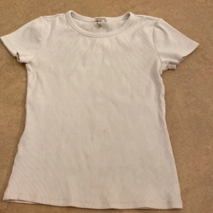 Vit ribbad t-shirt - Säljer en stilren vit ribbad t-shirt med korta ärmar. Perfekt basplagg för alla tillfällen. Skön och enkel att matcha med andra kläder. Lite fläckar. Passar för storlek s och xs