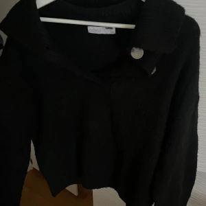 Svart stickad tröja  - Säljer en svart stickad tröja med en unik krage och knapplösning. Tröjan har långa ärmar och en stilren design som passar perfekt för kyligare dagar. Perfekt för dig som vill ha något både bekvämt och snyggt! Storlek xs men passar även större storlekar!