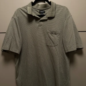 Grön pikétröja från Van Heusen - Säljer en stilren grå pikétröja från Van Heusen. Tröjan har korta ärmar och en klassisk krage med knappar. Perfekt för en avslappnad men ändå snygg look. Klippt snyggt så den är bra längd 