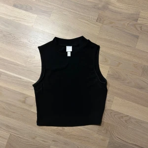 Svart ärmlös topp - Snygg svart ärmlös topp med hög hals. Perfekt för lager-på-lager eller som den är. Enkel och stilren design som passar till många olika outfits.