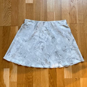 Festlig vit/grå kjol med mönster från Weekday - Snygg vit kjol från Weekday med ett subtilt mönster. Perfekt för en stilren look. Tillverkad i ett lätt och bekvämt material.