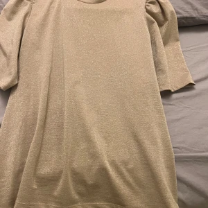 Beige glittrig blus - Snygg beige blus med glittrigt material och trekvartsärmar. Perfekt för en elegant look.