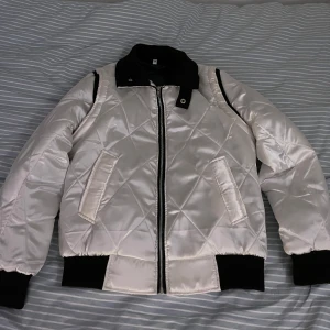 Vit bomberjacka  - Snygg vit quiltad bomberjacka med svart krage och muddar. Jackan har en broderad skorpion. Nypris 1000kr. Bara använd 2 gånger så inga tecken på användning. 