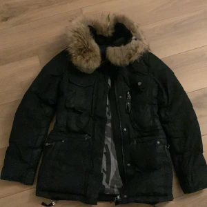 Svart vinterjacka med pälsdetaljer - Säljer en snygg och varm svart vinterjacka med pälsdetaljer på huvan. Jackan har flera praktiska fickor och en dragkedja framtill. Perfekt för kalla vinterdagar! 🖤Hollister jacka strl 34