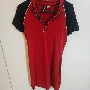 Röd och svart klänning med dragkedja - Säljer en röd tajt klänning med svarta korta ärmar och en dragkedja framtill.