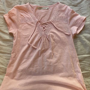 Rosa topp med spetsdetaljer från Lorie for her - Säljer en söt rosa topp från Lorie for her i storlek XS. Toppen har korta ärmar och fina spetsdetaljer vid halsen. Den har också en snygg knytning framtill som ger en extra touch. Perfekt för vår och sommar!