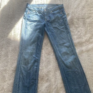 Blå jeans med guldbroderi - Säljer ett par snygga Victoria Beckham jeans i färgen blå med kronor av färgen gul/guld  på bakfickorna. 