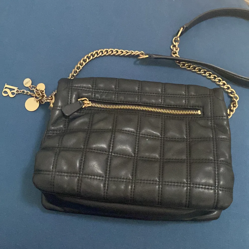 Säljer en snygg svart quiltad axelväska från Guess. Väskan har en elegant kedjerem i guld och flera små detaljer som Guess-loggan och charmiga hängen. Insidan är fodrad med Guess-mönster och har flera fack för bra organisering. Perfekt för både vardag och fest!. Laukut & Käsilaukut.