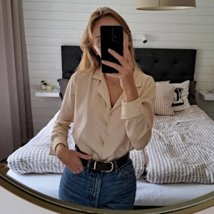 Sidenblus från Chiquelle - Beige/ljusgul sidenblus från Chiquelle i storlek XS. Den är i fint skick bortsett från en liten, ljus fläck på ena armen (se sista bilden). Kan eventuellt gå att få bort med fläckborttagning (har ej testat) men annars inget man tänker på.