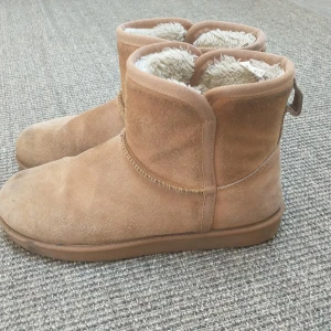 Bruna mocka boots med foder - Säljer ett par mysiga bruna skor i mocka med mjukt foder inuti. De har en enkel design med en liten flik bak för att lättare ta på sig dem. Skorna är välanvända med några märken på ytan, men går helt bra att använda hör av er om frågor!Nypris: 500kr
