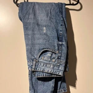 Blå jeans med slitningar - Säljer ett par klassiska blå jeans med coola slitningar. Perfekta för en avslappnad och trendig look. De har en normal passform och är gjorda av slitstarkt denim. Perfekta för vardagsbruk!