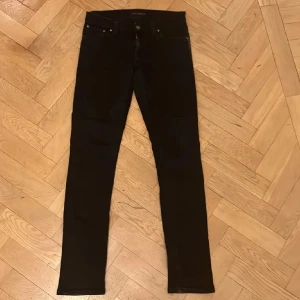 Nudie Jeans - Snygga svarta jeans med en klassisk slim passform. Byxorna har dragkedja och knappar framtill samt fickor både fram och bak.  W27-L30 166cm