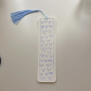 Bokmärke med blå rosetter och tofs - Charmigt bokmärke dekorerat med små blå rosetter och en matchande blå tofs. Perfekt för att hålla koll på var du är i din bok. Tillverkad i ett lätt och hållbart material. Tofsen går även att byta färg på om så önskas!