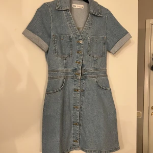 Jeansklänning från Zara - Snygg jeansklänning från Zara i en klassisk blå denim. Klänningen har korta ärmar med uppvikta kanter och knappar framtill. Två bröstfickor och två fickor bak ger en cool look. Perfekt för en avslappnad stil. Endast testad!!❤️❤️