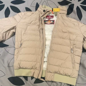 Beige dunjacka Parajumpers  - Snygg PJS dunjacka från Parajumpers med dragkedja och ribbade muddar. Perfekt för kyliga dagar med sin quiltade design och praktiska fickor. En stilren jacka som håller dig varm och bekväm.  Jackan är en barnstorlek i storlek S.