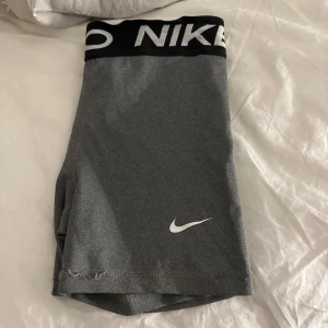 Grå träningsshorts från Nike - Snygga grå träningsshorts från Nike med en elastisk midja och logga i vitt. Perfekta för gymmet eller löprundan. Bekväma och stilrena med en tight passform. Sömmarna på benen är lite spruckna men trådar inte eller så!!