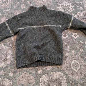 Grå ulltröja från Peak Performance - Säljer en grå ulltröja från Peak Performance med ett diskret mönster i vitt över bröstet och ärmarna. Tröjan har en ribbad krage och långa ärmar, perfekt för kyliga dagar. Den är tillverkad av 100% ren ull vilket gör den både varm och bekväm. Och är mindre i storleken 