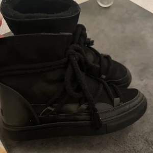 Svarta Inuikii boots  - Snygga svarta boots med hög skaft och snörning. Skorna har en robust sula och är tillverkade i  mocka. Perfekta för kyligare väder med en stilren design. Använda men fortfarande i fint skick, liten inböjning vid hälen men inget som påverkar skon