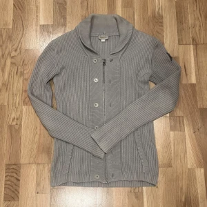 Diesel kofta - Säljer en stilren grå ribbad kofta från Diesel. Koftan har långa ärmar, knappar och dragkedja framtill. Perfekt för lager-på-lager under kyligare dagar. En klassisk och tidlös design som passar till det mesta.