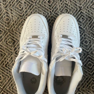Vita Nike Air Force sneakers - Säljer ett par klassiska vita Nike Air Force sneakers. De har en stilren design med snörning och perforerade detaljer på ovansidan för ventilation. Perfekta för en casual look.