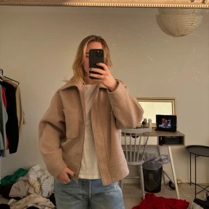 Beige jacka från NA-KD - Säljer en snygg beige jacka från NA-KD. Jackan har en dragkedja framtill och stora fickor på bröstet. Den är långärmad och har en klassisk krage. Perfekt för höst och vår