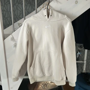 Beige hoodie från Nike - Säljer en stilren beige hoodie från Nike med en klassisk känguruficka och justerbar huva. Perfekt för en avslappnad look. Den har en liten Nike-logga på bröstet.