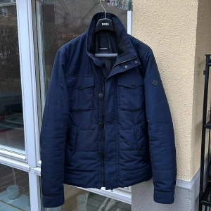 Mörkblå jacka från J.Lindeberg - Säljer en stilren mörkblå jacka från J.Lindeberg. Jackan har en quiltad design med dragkedja och knappar framtill. Perfekt för höst och vår med sin långa ärmar och praktiska fickor. Det finns däremot ingen knapp längst ner men syns inte när man har på sig jackan då knappen är längst ner. Ny pris 1800kr 