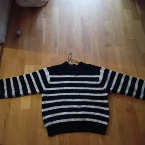 Svart och vit randig stickad tröja - Säljer en svart och vit randig stickad tröja med långa ärmar. Perfekt för kyliga dagar och ger en klassisk look. Tröjan har en enkel design med horisontella ränder och en rund halsringning.