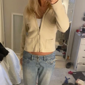 Beige kofta från Flash - Säljer en beige kofta från Flash med dragkedja framtill. Koftan har långa ärmar och två fickor!