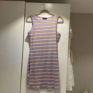 Randig ärmlös klänning från Shein - Säljer en färgglad randig klänning från Shein i storlek S. Klänningen är ärmlös och har en ribbad textur med ränder i blått, rosa, gult och lila. Perfekt för en somrig look! Som ny