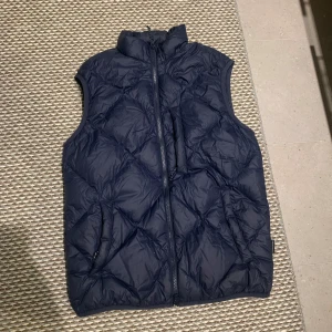Mörkblå dunväst från Peak Performance - Säljer en snygg mörkblå dunväst från Peak Performance. Västen har en quiltad design och en praktisk dragkedja framtill. Säljer västen då den växt ut mig. Tveka inte att höra av er vid intresse  skick är ungefär 8,5 av 10. Köpte den runt 2000 
