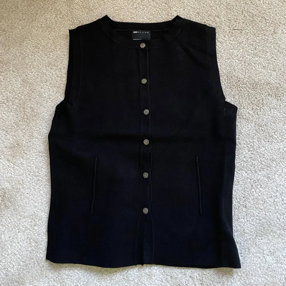 Snygg svart väst från Massimo Dutti med knappar framtill. Perfekt för en stilren look. Västen har en klassisk design med rund hals och två fickor.. Neuleet.