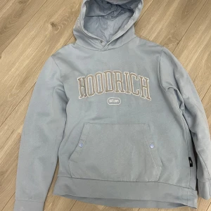  Hoodrich hoodie  - Säljer en stilren blå hoodie från Hoodrich med tryck både fram och bak. Den har en stor ficka framtill och en bekväm huva. Perfekt för en avslappnad stil.