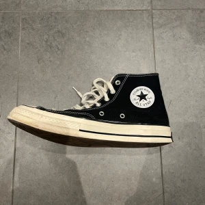 Converse Chuck 70 - Klassiska svarta Converse All Star sneakers med hög snörning och vit sula. Skorna har den ikoniska logotypen på sidan och är perfekta för en avslappnad stil. Inuti vänster sko så har lite tyg lossnat vid ovansidan av hälen typ, men inget som syns. Storlek 43. 