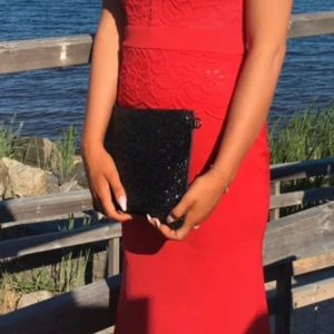 Röd långklänning med spetsdetaljer - Säljer en elegant röd långklänning med vackra spetsdetaljer. Klänningen har en tight passform och är perfekt för festliga tillfällen. Den är ärmlös och har en stilren design som framhäver figuren. Perfekt för sommarens alla fester!