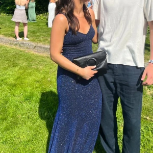 Balklänning glittrig - Mörkblå balklänning som glittrar i olika färger i solsken. Glittret är insytt i tyget så det ramlar ej av. Svart innertyg. Är 163 cm och har 11 cm klackar på bilderna. Hög slits.