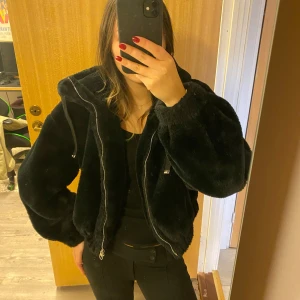 Svårt pälsjacka🖤🖤 - Säljer en supermysig svart fusk pälsjacka från Bershka. Den har en dragkedja framtill och en stor huva som sitter perfekt. Jackan är i ett superfint skick då den endast använts ett fåtal gånger. Pälsen är fortfarande jätte mjuk, förutom längs dragkedjan och resåren där den är lite mindre mjuk. Den passar perfekt att mysa i under hösten och vintern. Den är både snygg och varm, perfekt för att hålla stilen när det blir kallt ute!!🌟Skriv för mer bilder/frågor.❤️❤️