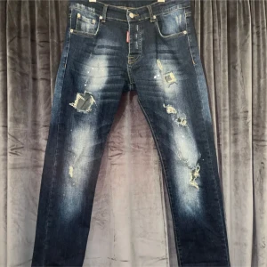 Mörkblå slitna jeans - Säljer ett par mörkblå jeans med coola slitningar och en vintage look. De har en klassisk femficksdesign och en knappgylf. Perfekta för en avslappnad stil med en touch av edge. Passar både till vardags och fest!