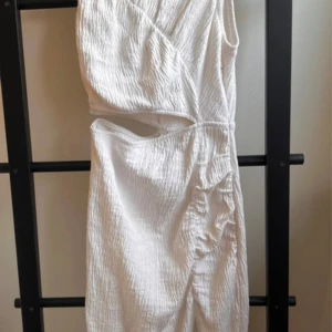 Vit omlottklänning  - Säljer en elegant vit omlottklänning med en unik struktur i tyget. Klänningen har en asymmetrisk design med oneshoulder-stil och är perfekt för sommarens fester. Materialet känns lätt och luftigt, vilket gör den idealisk för varma dagar. Passar både till vardag och festliga tillfällen!