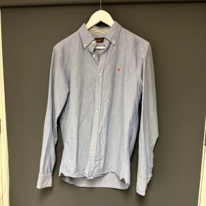 Blå skjorta från Morris - Säljer en stilren blå skjorta från Morris i storlek M. Skjortan har långa ärmar och knappar fram. Perfekt för både vardag och festliga tillfällen. Bra skick. 